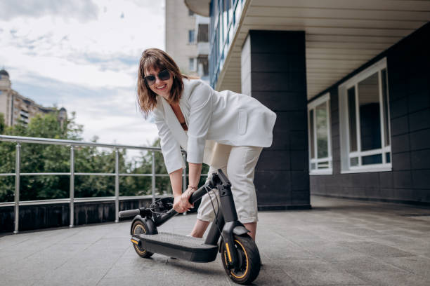 istock Pretty woman in white suit folding her electro scooter after ride while standing on background of modern building 1459774980