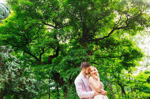 A close-up of a couple who gently embrace standing under a large green tree