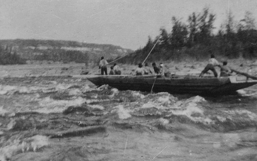 Group of men in a scow boat navigating the rapids on the Athabasca River in Alberta, Canada. Vintage photograph ca. 1915.