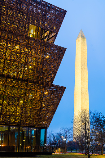 Washington D.C., USA - January 17, 2023: The National Museum of African American History and Culture at night with the Washington Monument in downtown Washington DC.