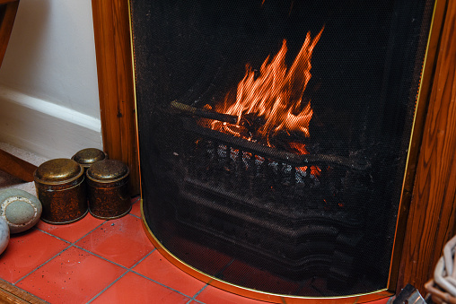 Woman putting a well dried log into a glowing wood burning stove.