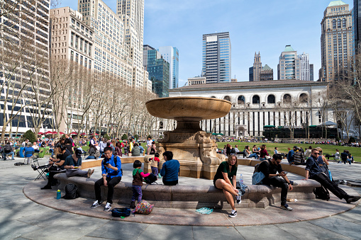 New York, USA - April 13, 2018: Group of business people sitting and having lunch in Bryant Park, Josephine Shaw Lowell Memorial Fountain is seen in foreground, Midtown Manhattan, New York City, United States.