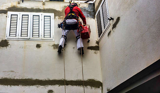 A painter.decorator painting a high wall, while strapped into a safety harness, Las Palmas, Gran Canaria