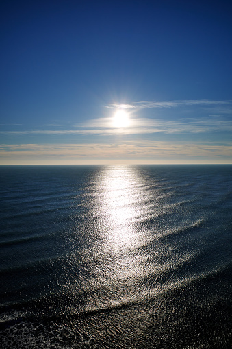 The sun is close to sunset over the boundless idyllic blue sea. Back lit. Blue sky and sea in half full. Sunlight reflection