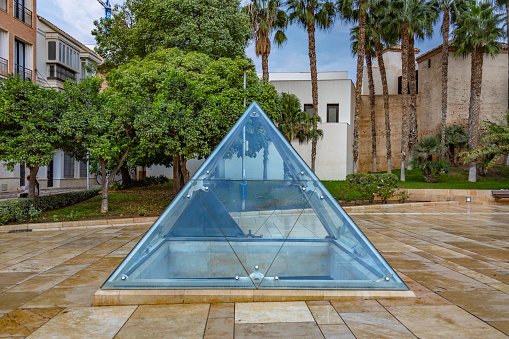 Cristal pyramid in a square at the front of  Roman Theater and Alcazaba citadel in Malaga, view at the C Alcazabilla avenue.