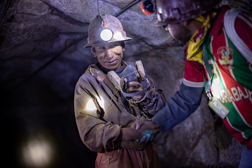 Fully equipped but friendly miner is shaking hands with a tour guide in the middle of the tunnel in Potosí, Bolivia
