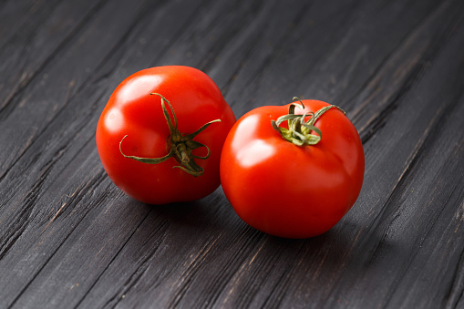 Two fresh ripe tomatoes on a dark wooden background close-up. Organic vegetarian product for a healthy diet.