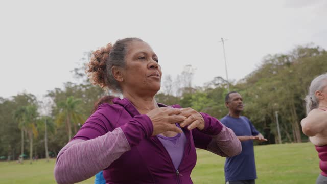 Senior woman doing breathing exercise with group class in a park