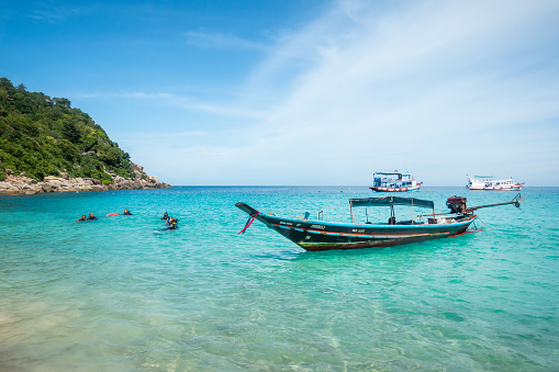 September 21, 2019 - Koh Tao, Thailand: People are getting diving lessons on Aow Luek bay beach with a Traditional wooden longtail boat and Thai Diving Ships in the background. Ko Tao is famous for its Dive Spots. Lots of tourists go on daily snorkeling and diving tours