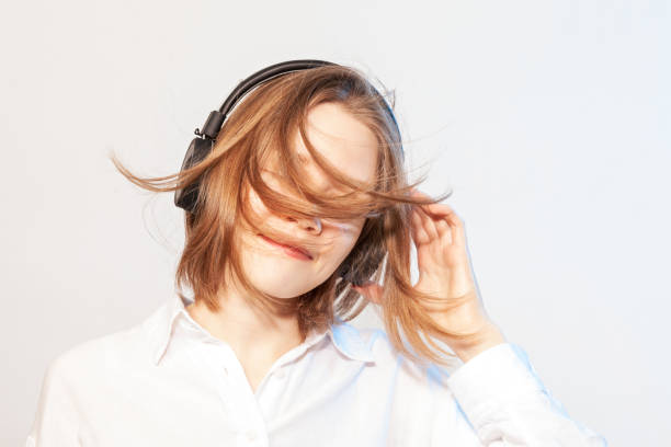 mujer asiática feliz de 22 años escuchando música con auriculares inalámbricos - blowing hair audio fotografías e imágenes de stock