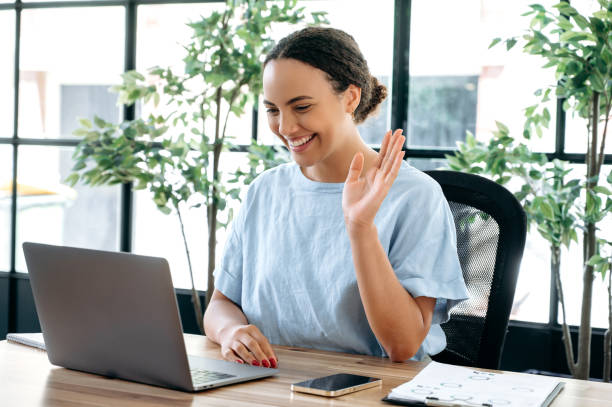 positive beautiful successful brazilian or latino woman, sits at a desk in the office, talking on video conference with a colleague or client, hiring manager conducts an interview with the candidate - speech recruitment technology young adult imagens e fotografias de stock