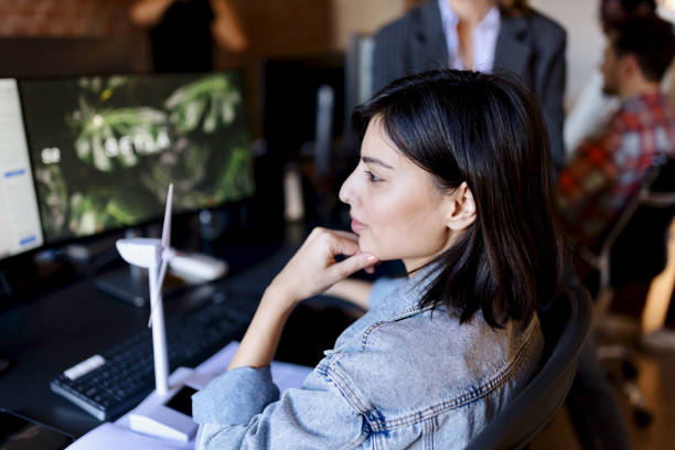 istock Businesswoman with blueprints on computer screen and wind turbine models 1459823604
