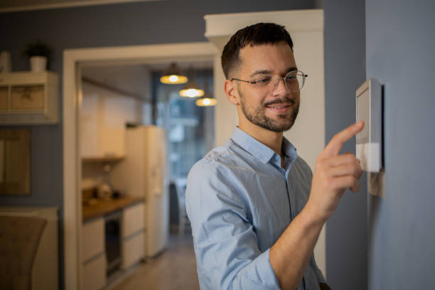 Young man adjusts the temperature at home with a device on the wall stock photo