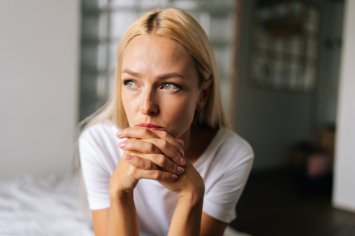 Closeup face of thoughtful woman sitting alone at home and looking away with sad expression holding hands on chin, thinking over problems. Frustrated female pondering make difficult choice.