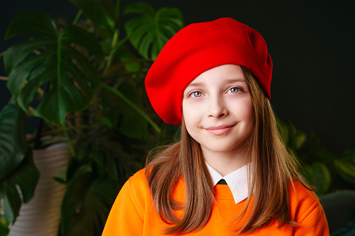 Teen smiling girl wearing red wool beret and orange sweater indoor. French style. Close up portrait