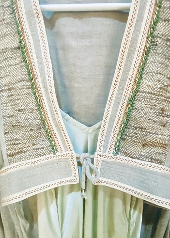 Vertical close up of hand made jacket made of hemp linen and cotton wool stitch on silk dress in neutral light pastel green tones