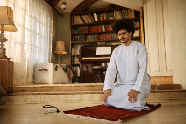 istock Young Muslim man sitting on prayer mat at home. 1459845914