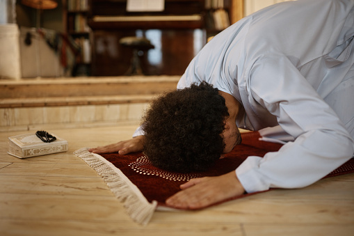 Muslim man praying in sajdah pose on a mat at home.
