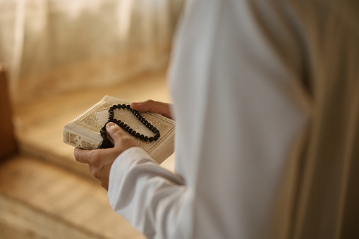 Close up of Arab man holding misbaha beads and Quran at home.