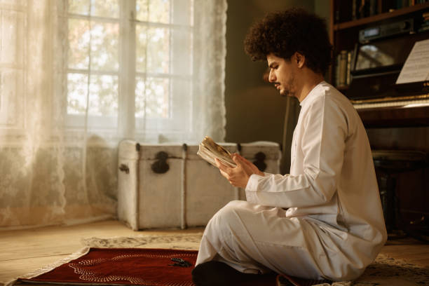 istock Middle Eastern man reading Koran while sitting on prayer mat at home. 1459846003