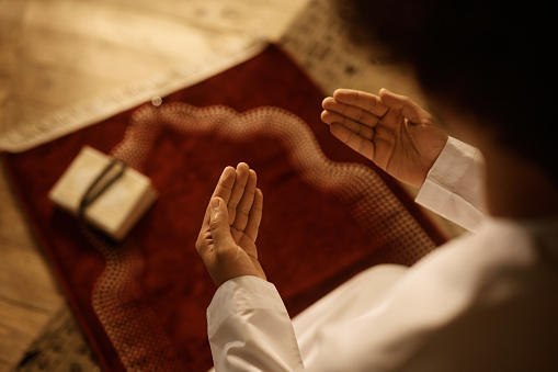 Close up of Middle Eastern man praying while sitting on traditional prayer mat at home.