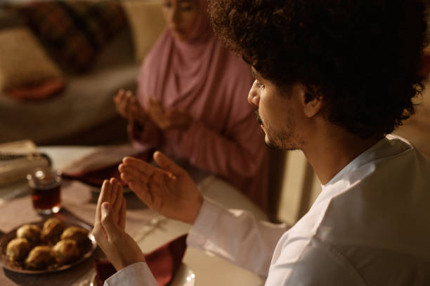 istock Close up of religious Arab couple praying at dining table. 1459846059