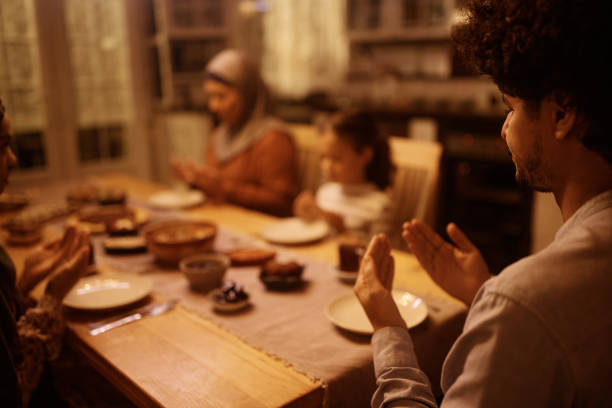 istock Close up of Middle Eastern man praying with his family during dinner at dining table. 1459846247