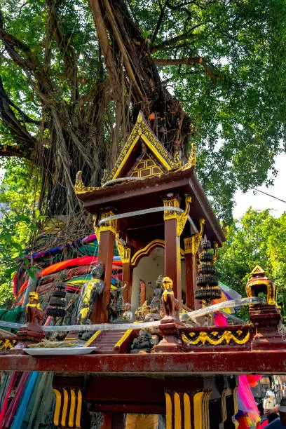 Photo of A spirit house with old banyan tree behind. Traditional
