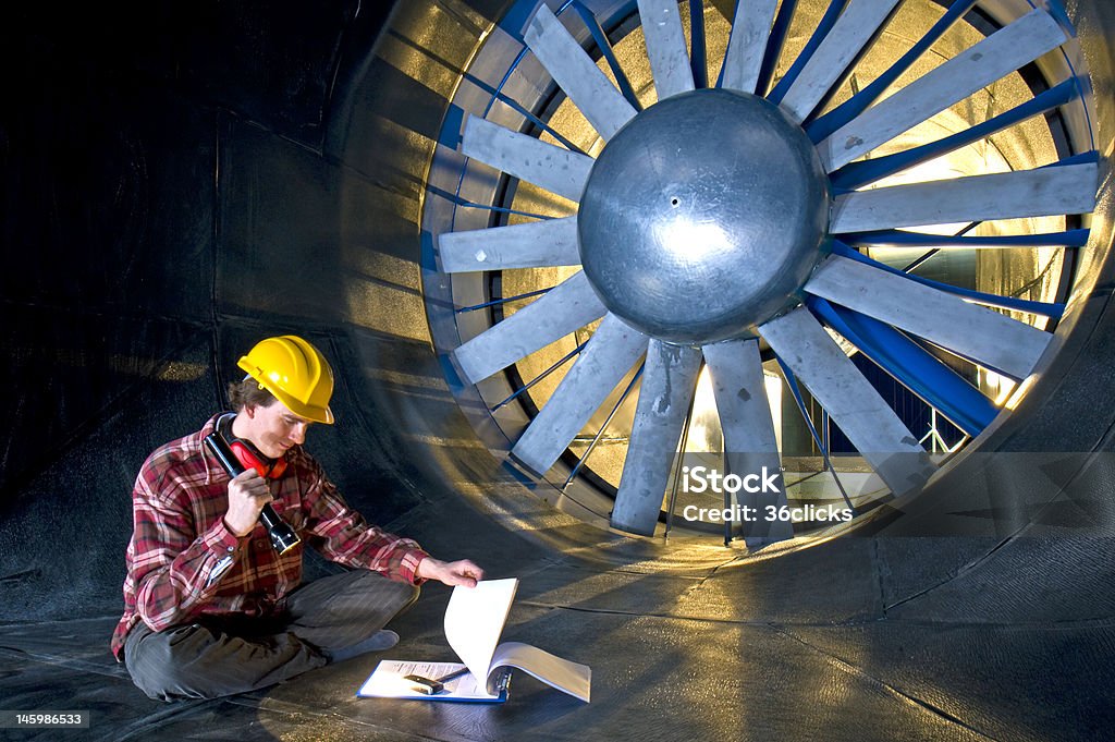 Engineer looking at his notes A young engineer, looking at his notes and wearing a yellow hardtop in side the realms of a backlit windtunnel Wind Tunnel Stock Photo