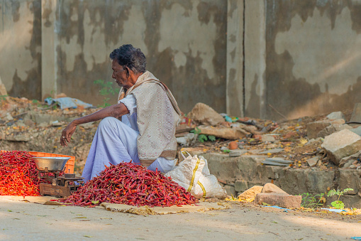 Puttaparthi, Andra Pradesh - India - January 21.2023: A man selling red chili pepers, sitting on the street at a local Indian market