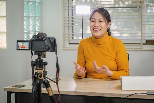 Asian woman vlogger live streaming from her office using camera tutorial video to social network by internet at home, Blogger and Customer engagement, Online-shopping and E-commerce, Influencer and Home Video Camera