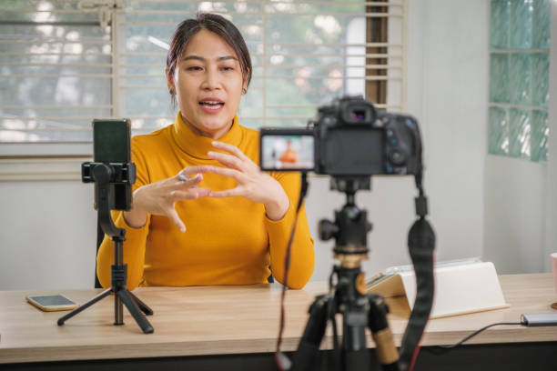 istock Asian woman vlogger live streaming from her office using camera tutorial video to social network by internet at home 1459869586