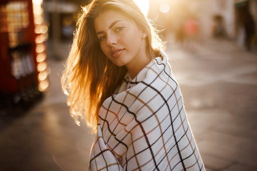 Beautiful young woman wrapped in scarf posing in the city at sunset