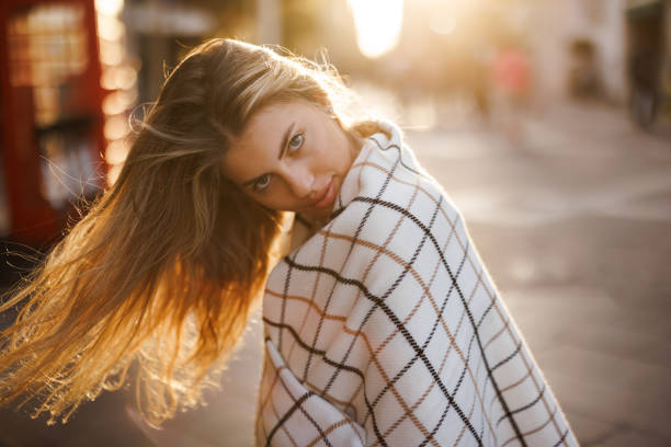 Beautiful young woman wrapped in scarf posing in the city at sunset