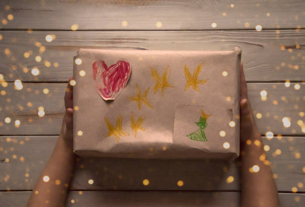 kind mit einem geschenk in kraftpapier eingewickelt, mit zeichnungen verziert - heart shape christmas paper christmas gift stock-fotos und bilder
