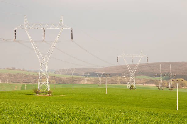 электричество pylons in green поля - power supply single line in a row sending стоковые фото и изображения