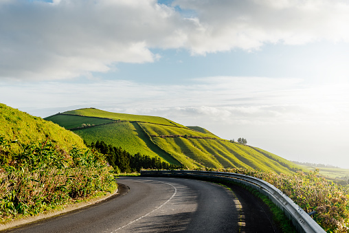 Driving scenic winding road on a sunny day through valley and green hills. Empty asphalt road leading into distance