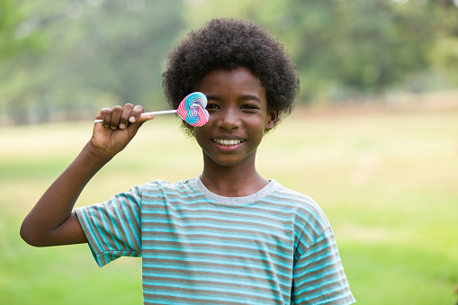 Smiling African American boy with colourful lollipops candy outdoor in the park. Happy child boy with lollipops candy outdoor
