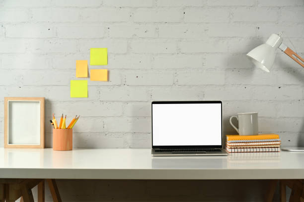 istock Creative workstation with laptop computer, pencil holder, books and lamp on white table. Empty screen for advertise design. 1459892276