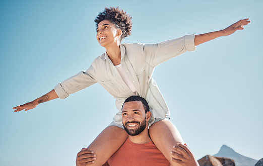 Love, happy and piggyback with couple and blue sky in nature for freedom, support and summer. Smile, vision and airplane with woman on man shoulders for vacation, bonding and affection together