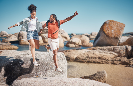 Black couple, fitness and beach while on vacation taking a jump or leap from a rock for travel, adventure and exercise in summer. Happy man and woman together at sea for quality time on holiday