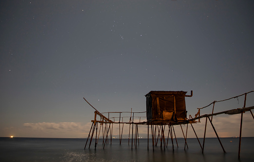 Night a starry sky with the constellation Orion and a fishing pier below