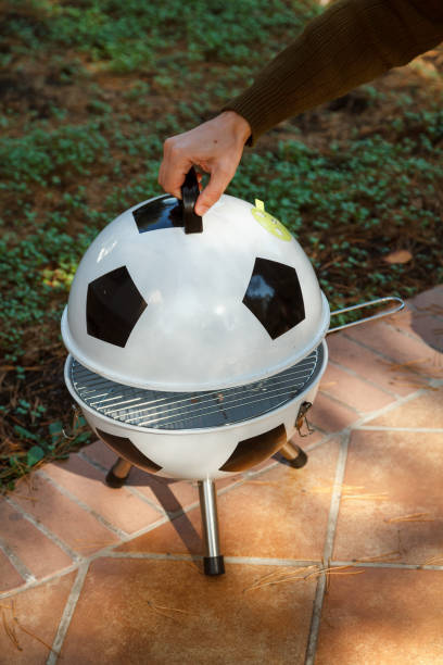 Hand open lid on round grill in yard