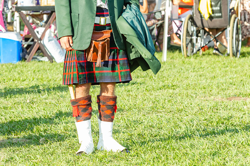 Scottish band musician unrecognizable member dress attire kilt colours  at highland games photograph outdoor field venue summer blue sky day.