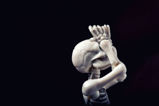 Skeleton figurine hold head by black background. Desperate figure on dark. Stressed and sadness doll, mental problems, feeling bad, depressed, disappointment, distressed, hopeless emotional concept