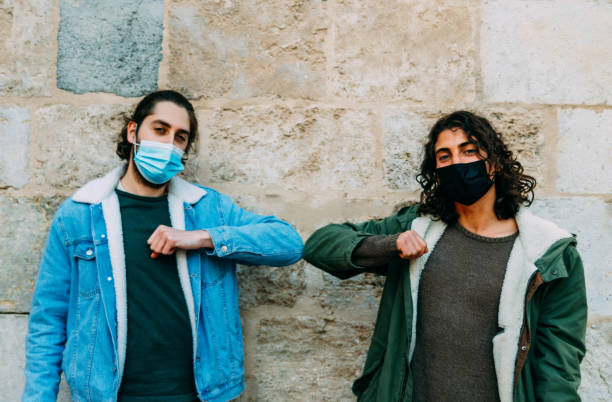 istock Young people in masks greeting each other with elbows- new normal concept 1459914620