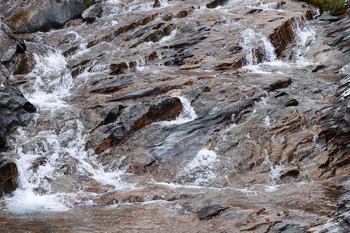 Beautiful texture of black-brown granite, saturated with various shades of minerals included in it, washed by the running water of an alpine stream. Aosta valley, Italy