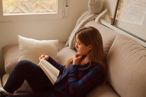 istock Blonde European female reading a book on a comfortable cream sofa 1459915652