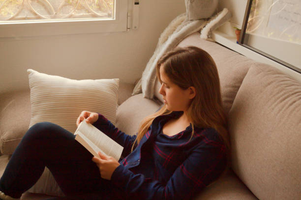 istock Blonde European female reading a book on a comfortable cream sofa 1459916377