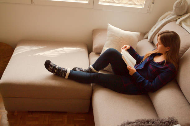 istock Blonde European female reading a book on a comfortable cream sofa 1459916383